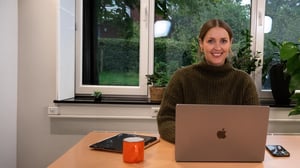 Eine Person sitzt in die Kamera lächelnd am Laptop