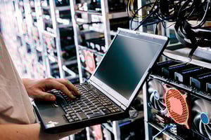 Mann steht am Laptop, der an Server angeschlossen ist